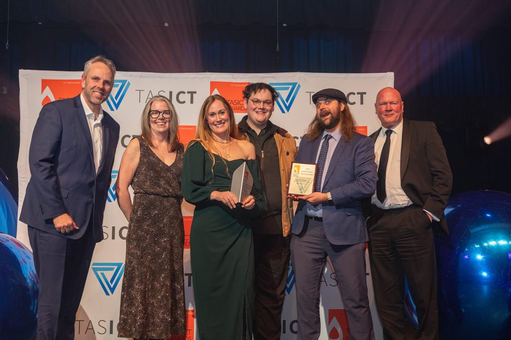 The Bank of us and Secret Lab teams on stage at the TasICT 2026 Excellence Awards, holding the Social Innovation Technology Award.