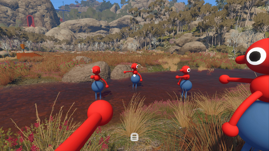 A first-person view in Big Walk: three red-and-blue characters with single large eyes stand in a shallow creek, surrounded by scrubby Australian bush, granite boulders and pink wildflowers, with a fourth character in the foreground. They're pointing at each other.