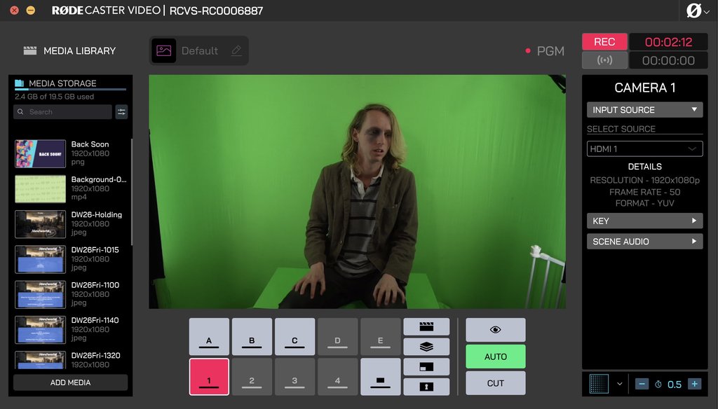 A video switcher interface with a program feed showing an actor in a jacket, with heavy dark eye makeup, sitting on a box in front of a green screen. The recording timer reads two minutes, and the media library on the left is full of /dev/world slides.