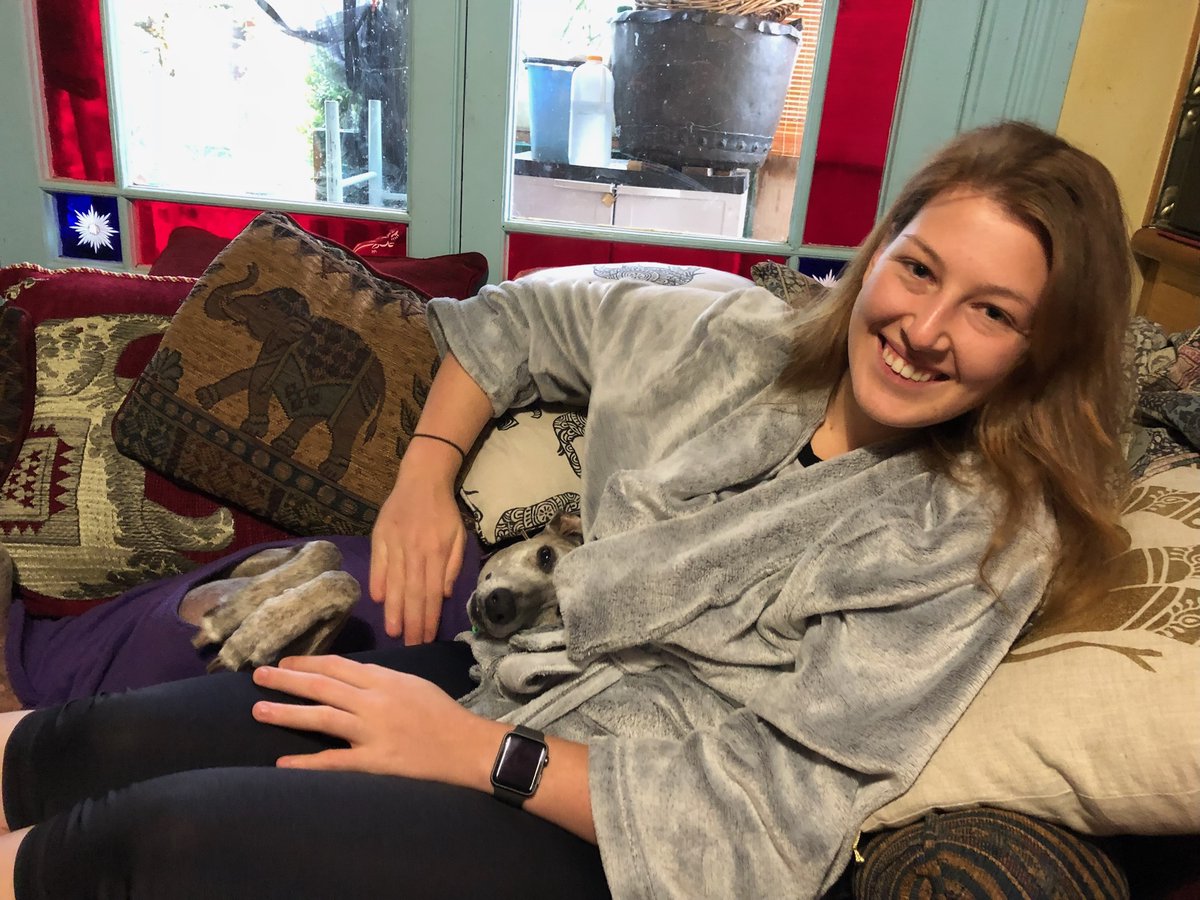 Mars smiling on a couch piled with patterned cushions, with Argos tucked in under Mars's grey dressing gown.