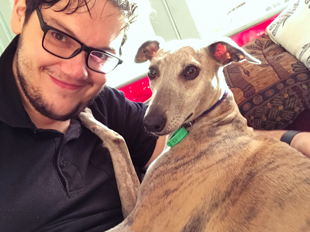 A selfie of Paris smiling on a couch, with Argos's paw resting on Paris's shoulder and Argos looking at the camera.